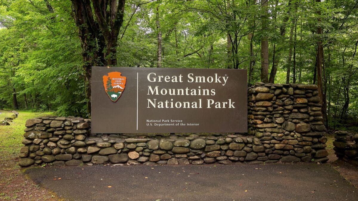 The wooden entrance sign for Great Smoky Mountains National Park surrounded by green trees and a stone base.