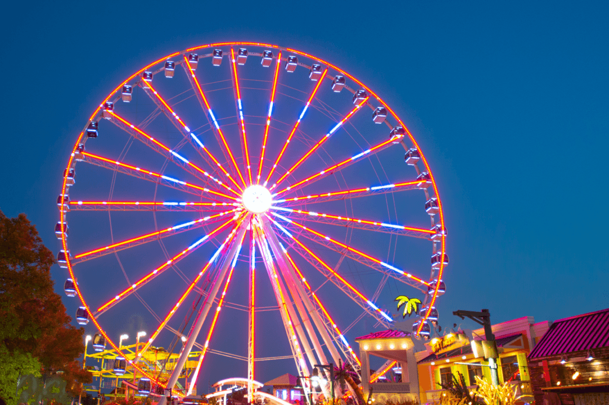 The Great Smoky Mountain Wheel at night, fully illuminated with bright red and blue neon lights against a dark twilight sky at The Island in Pigeon Forge.