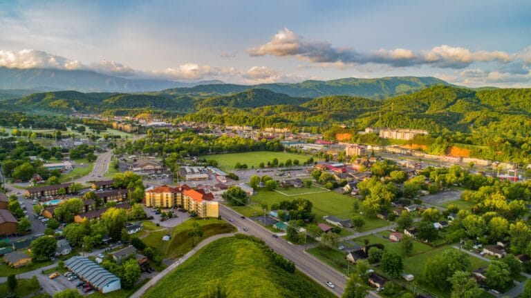 Aerial view of Pigeon Forge and Sevierville, Tennessee, showing hotels, roads, and green spaces nestled against the rolling green foothills of the Great Smoky Mountains.