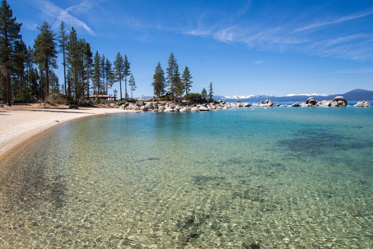 Shallow turquoise water and sandy beach at Sand Harbor State Park, Lake Tahoe, with granite rocks and pine trees.