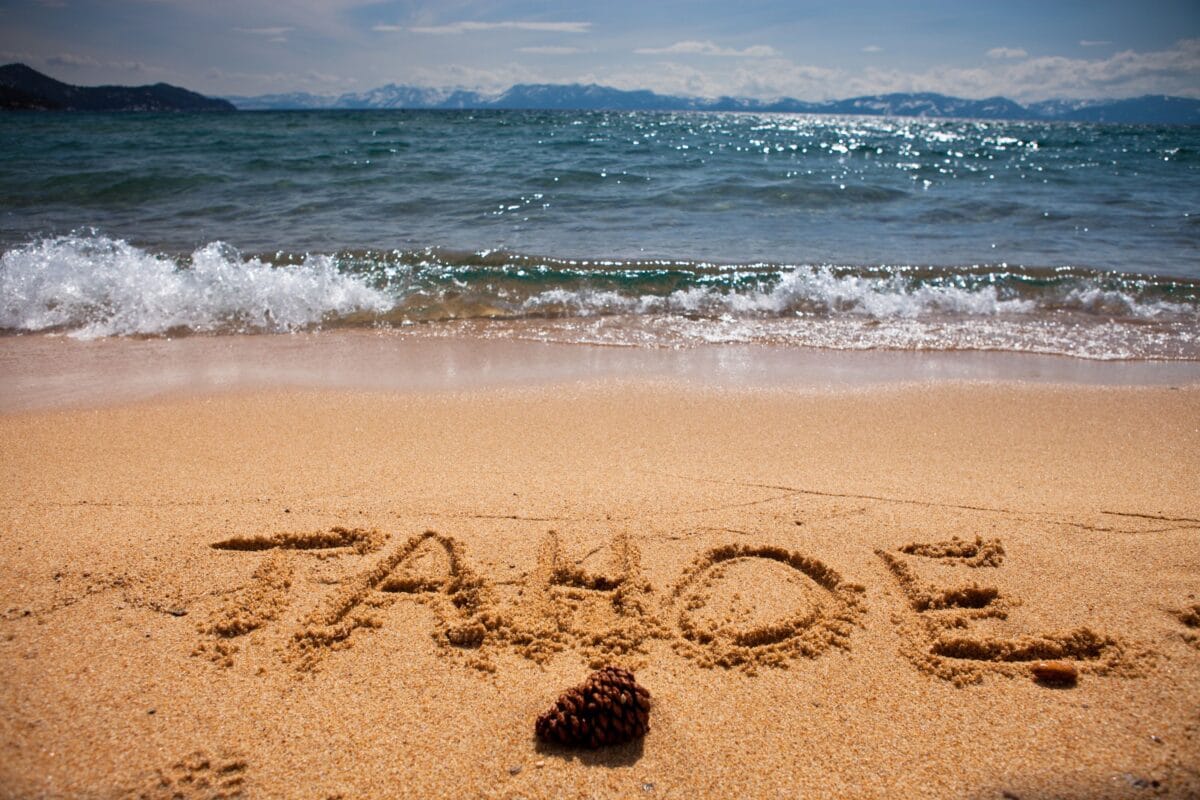 shoreline of Lake Tahoe beach with mountains in the distance. Tahoe written in the sand.