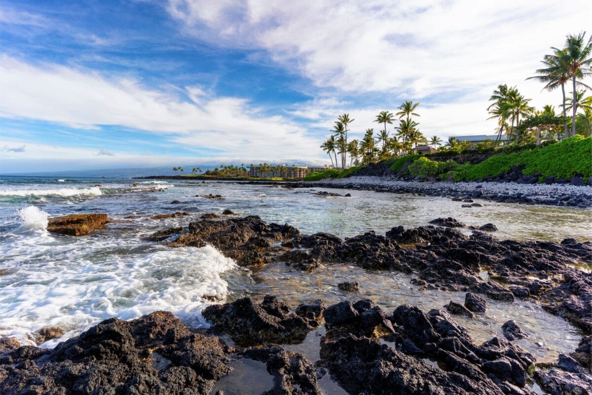 Rocky lava rock shoreline at Waiulua Bay in front of the Hilton Waikoloa Village resort on the Big Island of Hawaii, showing the typical volcanic coast and white waves.