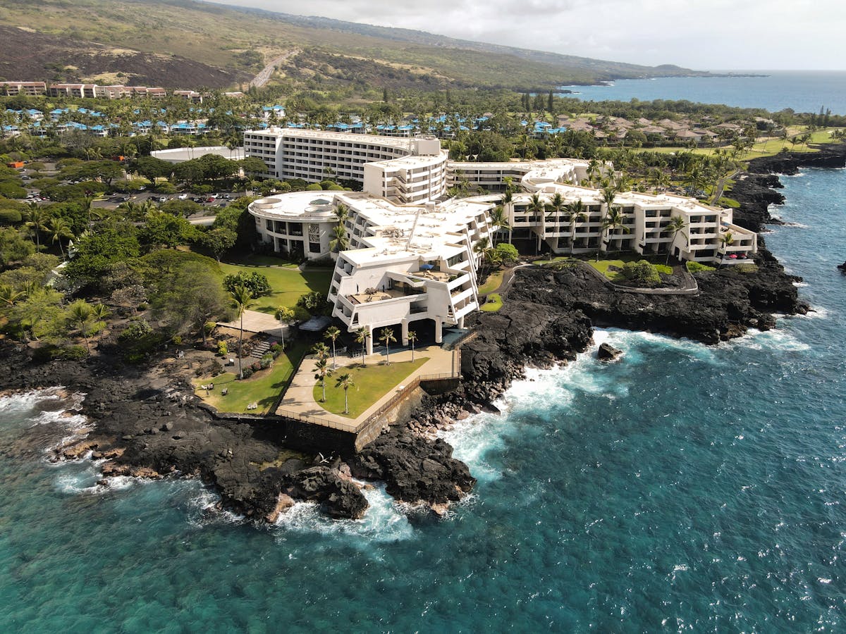 A stunning aerial view of a resort on the rocky coastline of Kailua-Kona, Hawaii, overlooking the Pacific Ocean.