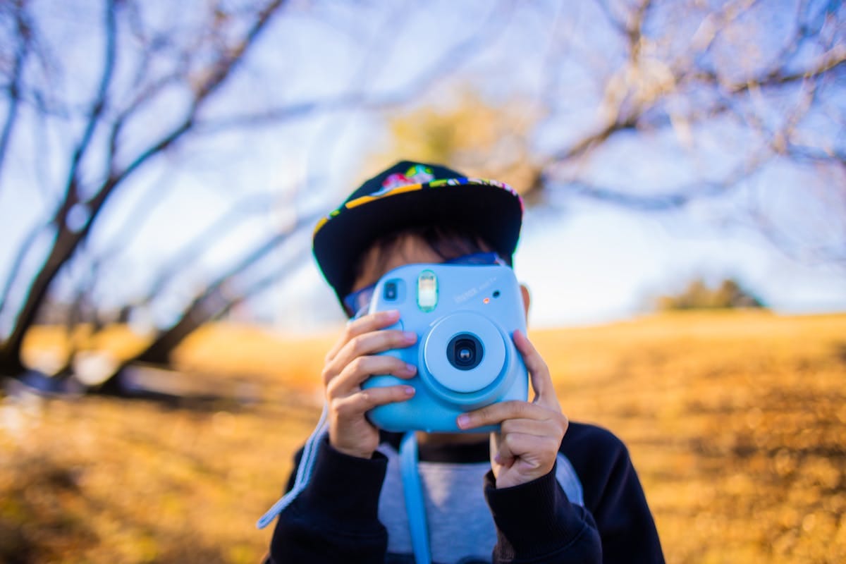 A young boy enjoys photography with an instant camera in a sunny outdoor park.