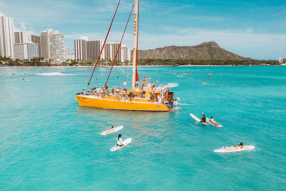 Aerial shot of surfers and catamaran near Waikiki Beach with Diamond Head in the background.