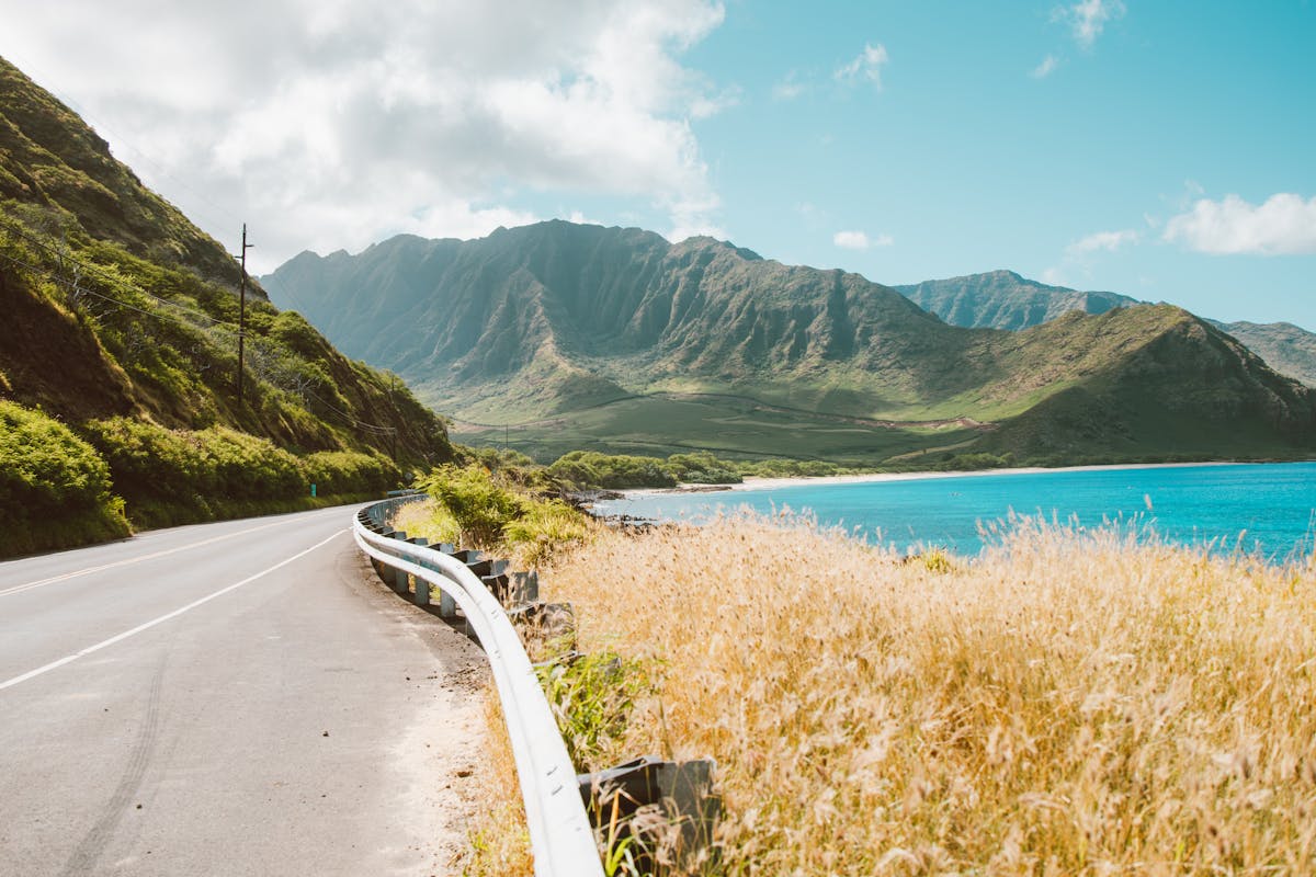 Beautiful view of a coastal road with lush Hawaiian mountains and clear blue waters.