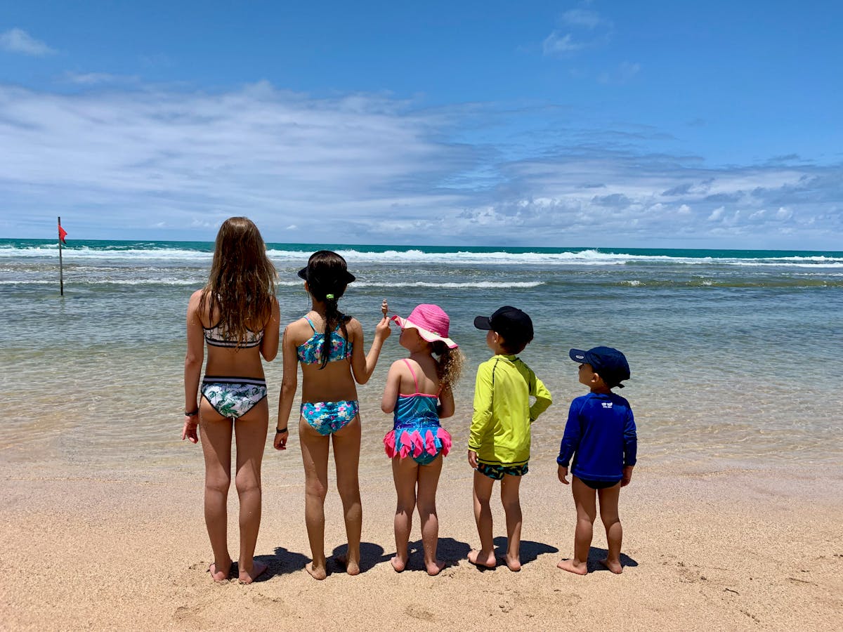 Group of children in colorful swimsuits enjoy a sunny day at the beach looking at the ocean.