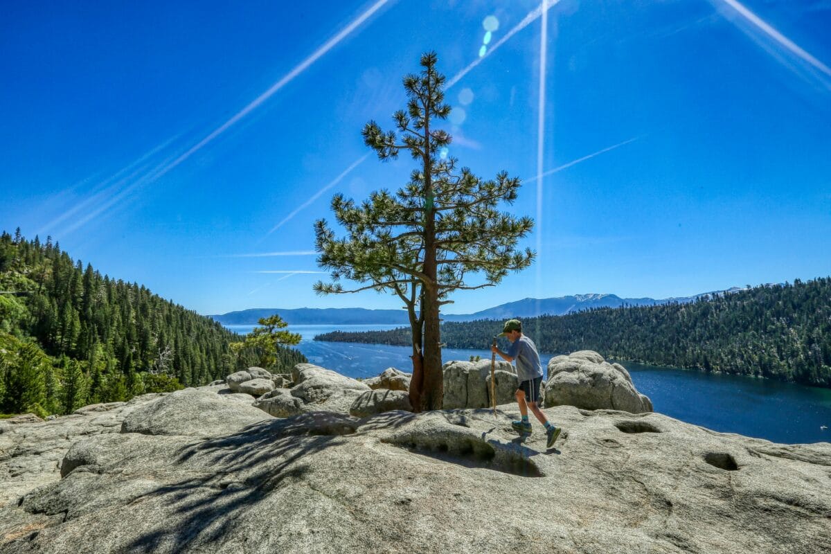 A young boy hiking on large grey boulders overlooking the deep blue water of North Lake Tahoe at the Monkey Rock vista point.