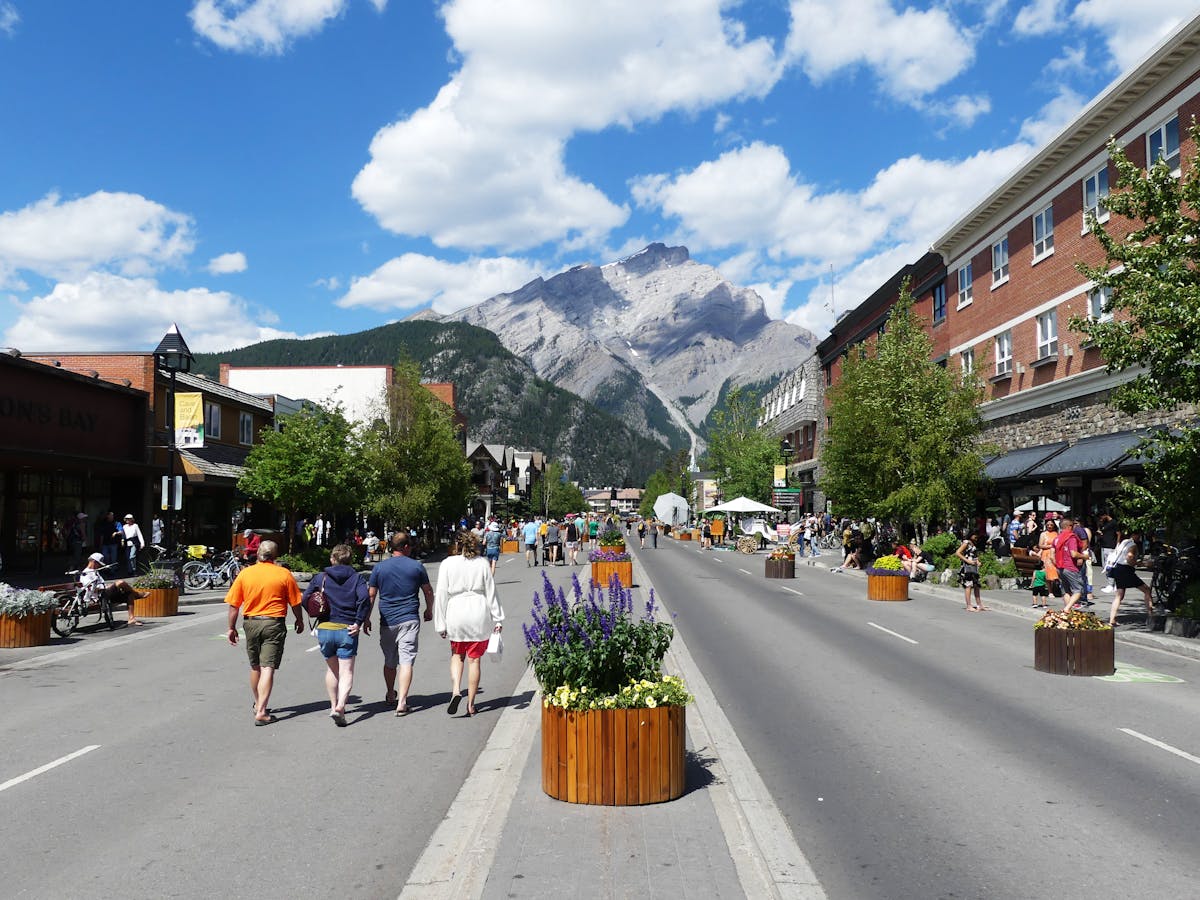 People walking along Banff Avenue with beautiful mountain backdrop on a sunny day.