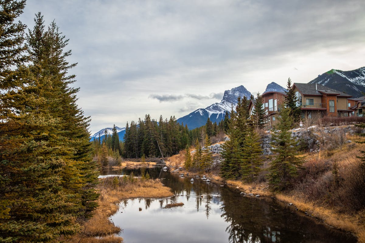 Picturesque view of river between trees and old building on hillside behind mountain under sky