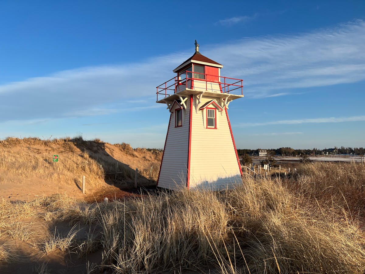 Best Places to visit in Canada with Kids 2 Rustic Covehead Harbour Lighthouse in Prince Edward Island, surrounded by dunes under a clear sky.