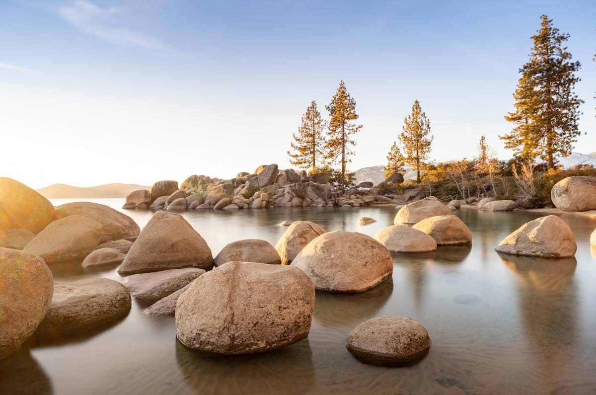 27 Best Things to Do in Lake Tahoe with Kids (Beaches, Hikes & Easy Family Activities) 3 Peaceful scene of Lake Tahoe at sunset with rocks and trees reflecting in the calm waters.