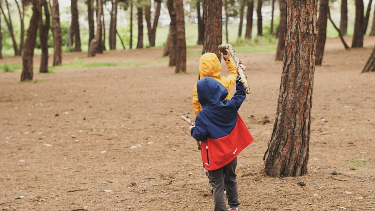 Two kids in jackets having fun playing in a forest clearing.